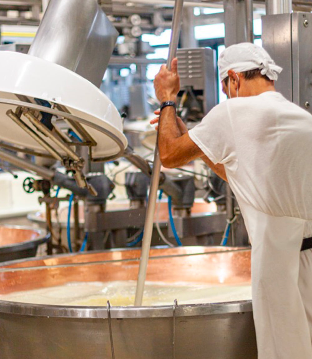 Operatore in caseificio che mescola il latte in una caldaia industriale